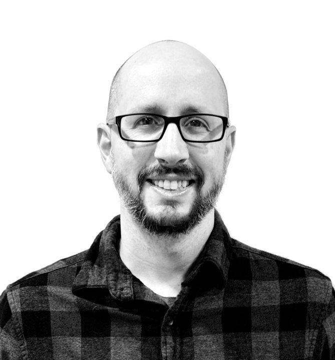 Kris Bader smiling, wearing glasses and a plaid shirt